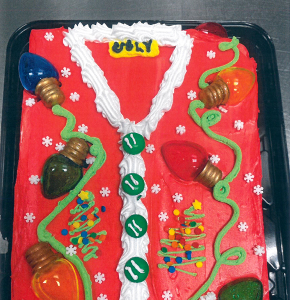 Overhead shot of a sheet cake decorated as a red Christmas sweater with Christmas lights.
